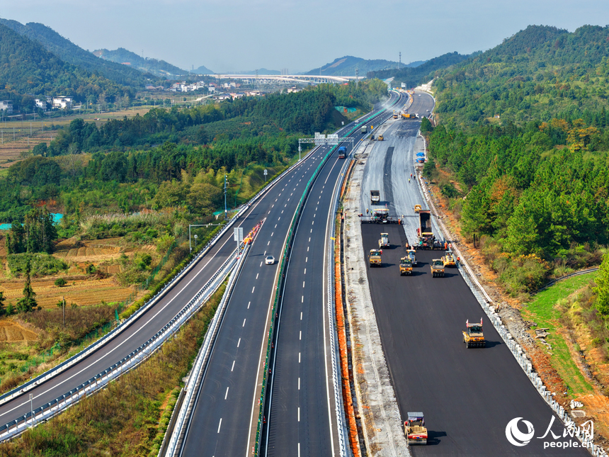 沪昆高速昌傅至金鱼石(赣湘界)段改扩建项目施工现场机械轰鸣,工人在摊铺路面沥青。人民网记者 朱海鹏摄